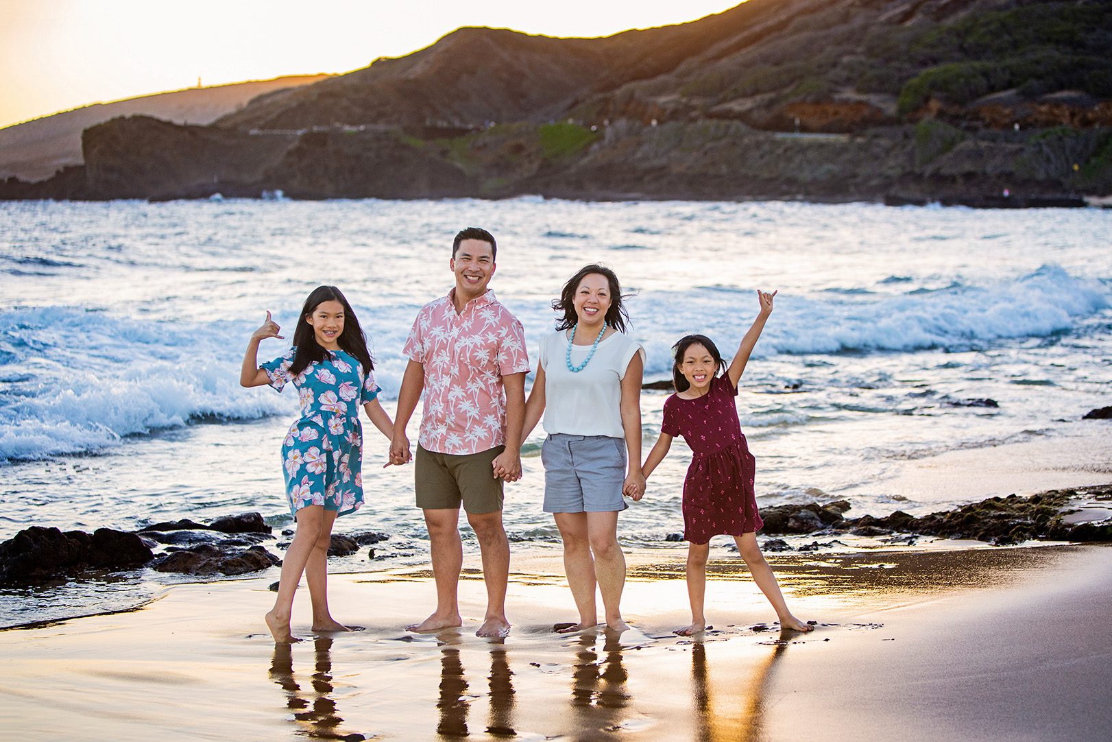 family posing for family photo at beeach in Hawaii at sunset