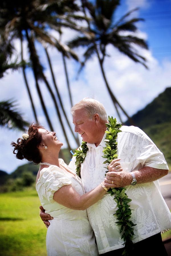 Mature bride and groom dance under palm trees at their Hawaii wedding.